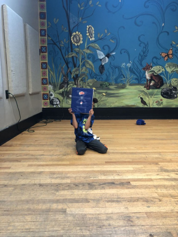 Person sitting in front of a room with a mural with plants and animals peeking around a blue 3-ring binder.